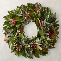 a green wreath with red berries and greenery hanging on a wall in front of a white background