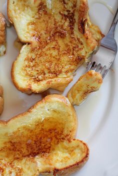 a white plate topped with french toast next to a fork and some other food items