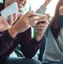 three people sitting down and looking at their cell phones while one person is holding an mp3 player