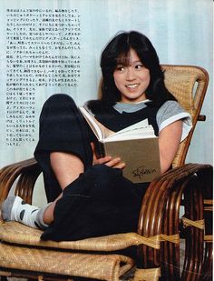 a woman sitting in a wicker chair holding a book and smiling at the camera