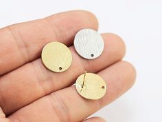 two small gold and silver disc earrings on a person's hand, one is facing the camera