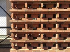 a large stack of red bricks sitting on top of a cement slab in front of a chain link fence