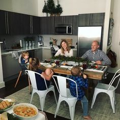 a group of people sitting around a kitchen table with food on top of the table