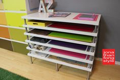 a white shelf with many different colored folders on it and a cell phone in the middle