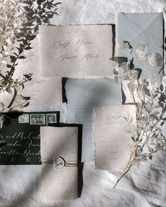 the wedding stationery is laid out on top of the bed sheet, with flowers and foliage