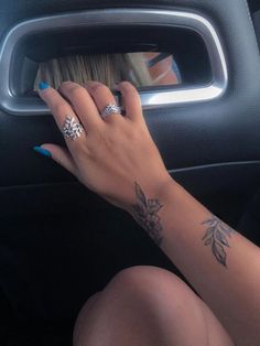 a woman's hand on the steering wheel of a car, with tattoos on her arm