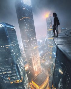 a man standing on top of a tall building in the middle of a city at night