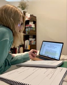 a woman sitting in front of a laptop computer on top of a desk next to a book shelf