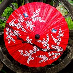 a red umbrella with white flowers on it sitting in front of a wooden fence post