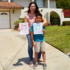 a woman standing next to a little boy holding up two signs in front of a house