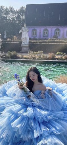 a woman in a blue dress is sitting on the ground near a fountain with flowers