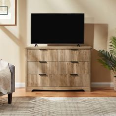 a flat screen tv sitting on top of a wooden dresser next to a chair and potted plant