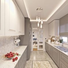 a long kitchen with white cabinets and marble counter tops, along with a bowl of fruit on the counter