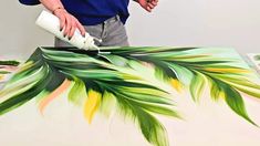 a man is painting leaves on a large piece of art with white paint and watercolors