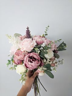 a person holding a bouquet of pink and white flowers with greenery in their hand