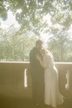 a man and woman standing next to each other in front of a tree filled park