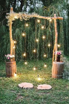 an outdoor ceremony with wooden barrels, string lights and flowers on the grass in front of it