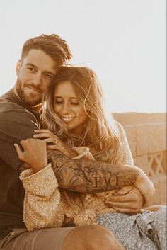 a man and woman hugging each other while sitting on top of a wooden bench in the sun