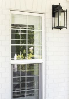 an open window on the side of a white brick building with a black light hanging from it