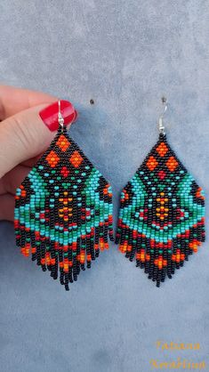 a pair of beaded earrings is being held by a woman's hand on a blue surface