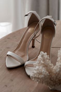 a pair of white high heel shoes sitting on top of a wooden table next to a bouquet