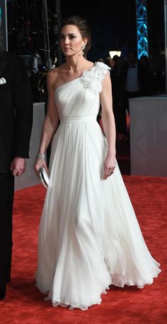 a woman in a white dress walking down a red carpet with a man in a tuxedo