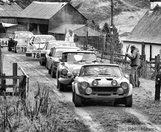 an old black and white photo of cars on a dirt road with people looking at them