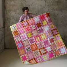 a woman holding up a large quilt in front of her face