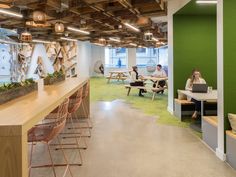 two people sitting at tables in an office with green walls and wood beams on the ceiling