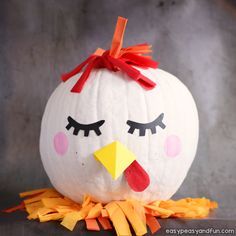 a white pumpkin decorated like a chicken with eyes and orange ribbon around its neck, sitting on a gray surface