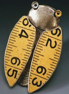 a pair of scissors sitting on top of a measuring tape shaped broochle in gold and silver