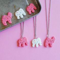 three pink and white elephant necklaces sitting on top of a metal tray next to a cookie sheet