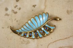 Circa 1930s/40s rhinestone and enamel pin on metal (not sure of content), gorgeous sky blue color with darker blue rhinestones, love the shape the leaf makesMeasures roughly 2.5" high x 1.25" at widestCondition: has a few light wear spots to enamel, back has one area of patina/wear near clasp, nothing serious Mid-century Blue Brooches For Gifts, Antique Blue Enamel Brooches, Art Deco Blue Brooches As Gifts, Art Deco Blue Brooches For Gifts, Vintage Blue Enamel Pin Gift, 40s Art, Sky Blue Color, Leaf Brooch, Blue Rhinestones