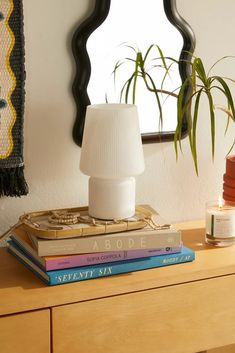 a stack of books sitting on top of a wooden table next to a lamp and mirror