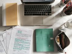 an open laptop computer sitting on top of a desk next to papers and pencils