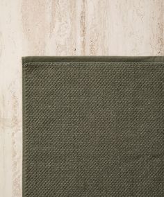 a close up of a green rug on a wooden floor with a white wall in the background