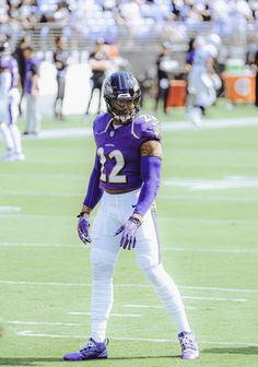 a football player is standing on the field with his hands in his pockets and wearing purple gloves