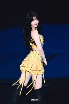 a woman with long black hair wearing a yellow dress and knee high boots on stage