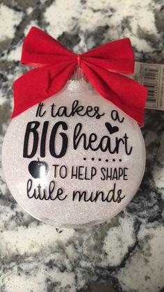 a white ornament with a red bow on it that says it takes a big heart to help shape little minds