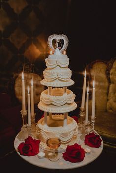 a white wedding cake with red roses and candles on the table in front of it