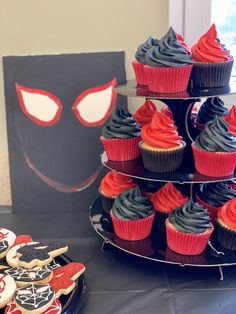 cupcakes and cookies are arranged on a table with a spiderman sign in the background