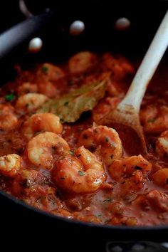 shrimp and tomato sauce being stirred in a skillet with a wooden spoon on the side