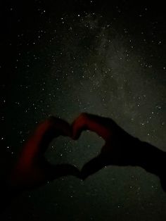 two hands in the shape of a heart against a dark night sky with stars above