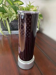 a purple vase sitting on top of a wooden table next to a potted plant