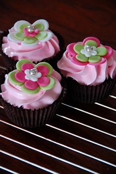 three cupcakes with pink frosting and flowers on them sitting on a cooling rack