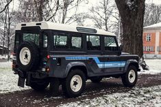 a black and white jeep parked in front of a tree with snow on the ground