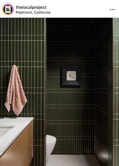 a bathroom with green tiled walls and white counter tops, along with a pink towel hanging on the wall