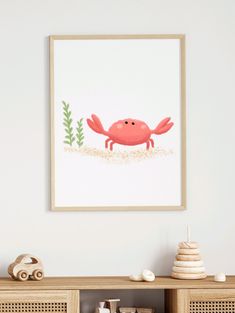 a crab is standing in the sand under a framed art print on a white wall