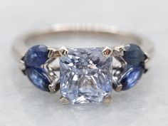 an engagement ring with three blue and white stones on the band, set in 18k white gold