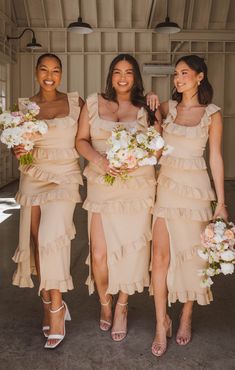 three bridesmaids in beige dresses holding bouquets and posing for the camera with their arms around each other